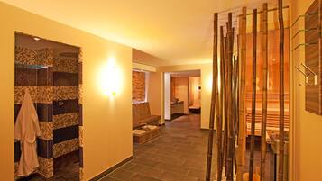 Enter a serene spa area with a mosaic-tiled wall, a wooden bench, and a bamboo screen leading to a sauna.