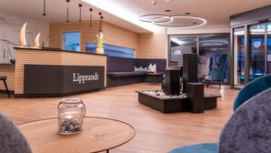 A modern reception area with a wooden reception desk labeled 'Lipprandt', a seating area with a sofa and chairs, and a decorative water feature. - Hotel Lipprandt (Wasserburg am Bodensee)