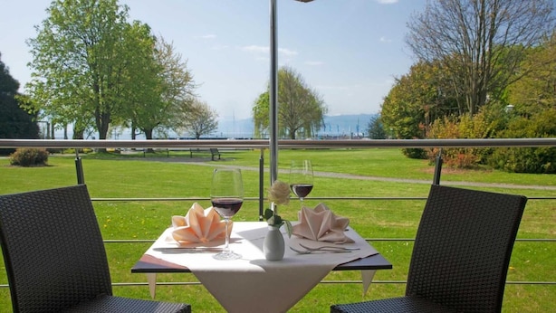 A table set with wine glasses and a vase of flowers, overlooking a scenic view of a lake and trees. - Hotel Lipprandt (Wasserburg am Bodensee)