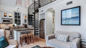 Una cocina moderna con una isla central, un área de comedor con sofá y sillas, una escalera y un ventanal con vistas.