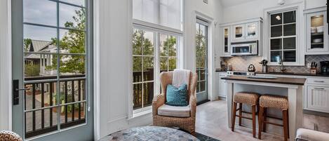 A spacious kitchen with large windows, a round dining table, and a wicker chair.