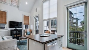 Un salón amplio con un gran ventanal, un televisor de pantalla plana, un sofá y una zona de comedor con una isla de cocina.