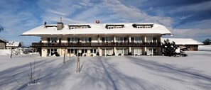 A large, multi-story building with a snow-covered roof and balconies, surrounded by snow. - Hotel Bergblick (Scheidegg)
