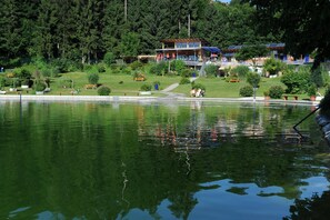 A lakeside hotel with a swimming area, outdoor seating, and a view of the forested hills. - Hotel Bergblick (Scheidegg)