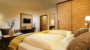 A hotel room with a wooden headboard, a flat-screen TV mounted on the wall, a desk with a chair, and a bed with white linens and decorative pillows.