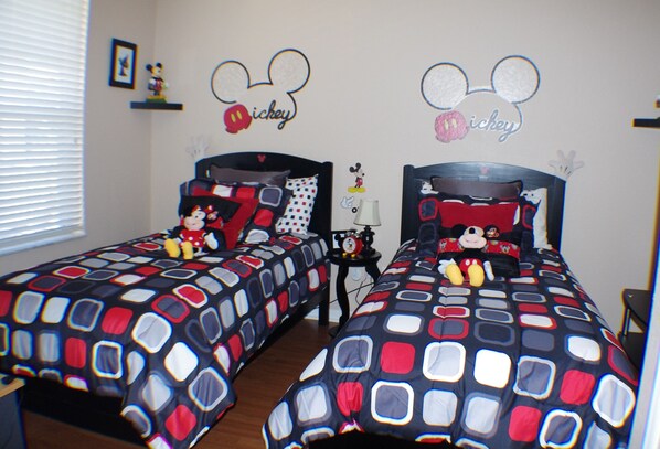 Une chambre avec deux lits, chacun agrémenté de draps et d’oreillers aux motifs de Mickey Mouse.