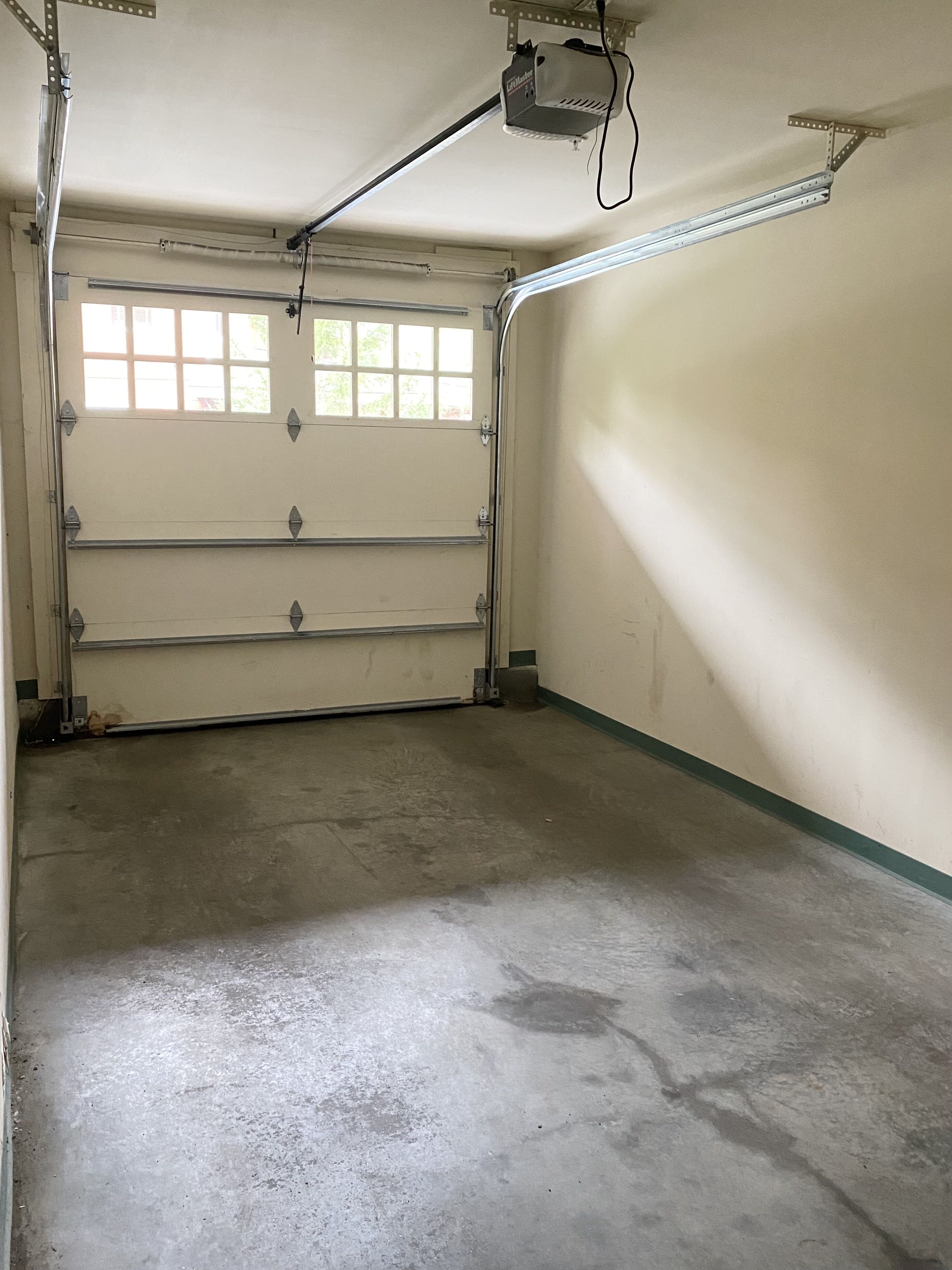 A garage with a concrete floor, a metal door, and a ceiling-mounted projector.