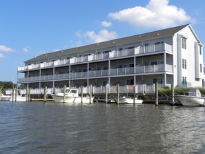 Un immeuble à plusieurs étages situé au bord de l’eau, doté de balcons, de bateaux amarrés et surplombant un ciel dégagé.