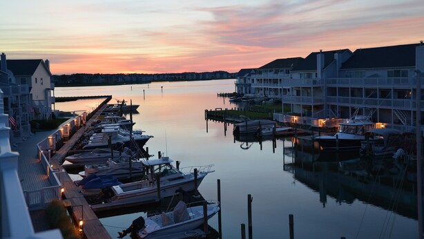 A marina with docked boats, waterfront buildings, and a calm sunset.