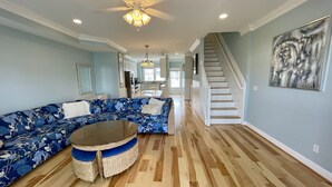 A spacious living room with a blue floral sofa, a round table, and a staircase leading to another level.