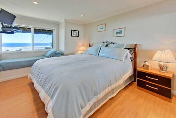 A bedroom with a large bed, a bedside table, a lamp, a TV mounted on the wall, and a window with a view of the ocean. - GREAT OCEAN VIEWS, LAST MINUTE DEAL!! BOOK NOW -BEAUTIFUL BEACH HOME!! (Watsonville)