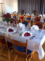 Un comedor con mesas redondas, sillas con cojines azules y rojos, y manteles blancos.