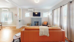 A modern living room with a fireplace, a sofa, and a flat-screen TV mounted above it. - Historic Bungalow w/porch, King1bd/1ba, Recently Renovated (Albuquerque)