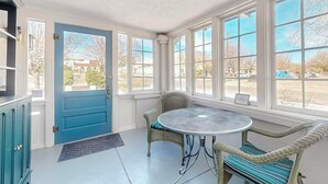 A room with a blue door, large windows, a round table, wicker chairs, and a view of a parking lot. - Historic Bungalow w/porch, King1bd/1ba, Recently Renovated (Albuquerque)