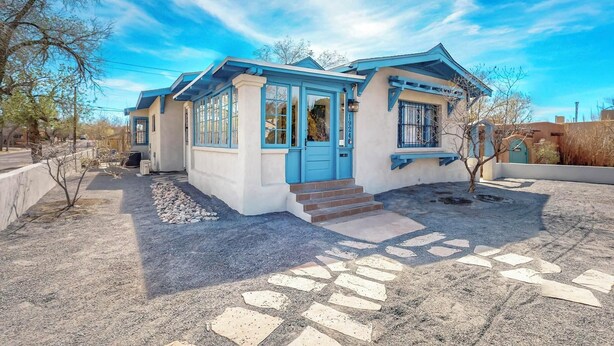 A two-story house with a blue door and windows, a small porch, and a gravel driveway. - Historic Bungalow w/porch, King1bd/1ba, Recently Renovated (Albuquerque)