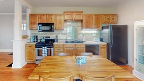 A kitchen with wooden cabinets, a stainless steel refrigerator, a microwave, and a dining table. - Historic Bungalow w/porch, King1bd/1ba, Recently Renovated (Albuquerque)