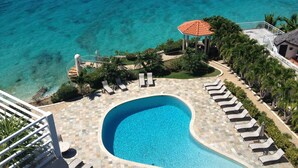 A swimming pool with a curved design, surrounded by lounge chairs and a gazebo. - Oceanfront Spectacular Penthouse W/Spacious Rooftop Terrace, Cupecoy Beach (Cupecoy)