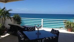 An outdoor patio with a table and chairs, overlooking a turquoise sea and a white railing. - Oceanfront Spectacular Penthouse W/Spacious Rooftop Terrace, Cupecoy Beach (Cupecoy)