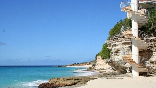 A spiral staircase leading up a rocky cliffside, overlooking a beach with clear blue water. - Oceanfront Spectacular Penthouse W/Spacious Rooftop Terrace, Cupecoy Beach (Cupecoy)