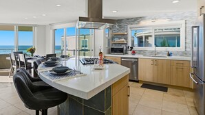 A modern kitchen with a large island, stainless steel appliances, and a view of the ocean. - Rockaway Oceanfront 2 | Lg Terrace- 4BR (San Diego)