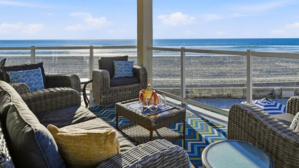 A balcony with wicker furniture, a glass table, and a view of the beach. - Rockaway Oceanfront 2 | Lg Terrace- 4BR (San Diego)