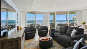 A modern living room with a large window offering a view of the ocean. There is a sofa, two armchairs, and a coffee table. - Rockaway Oceanfront 2 | Lg Terrace- 4BR (San Diego)