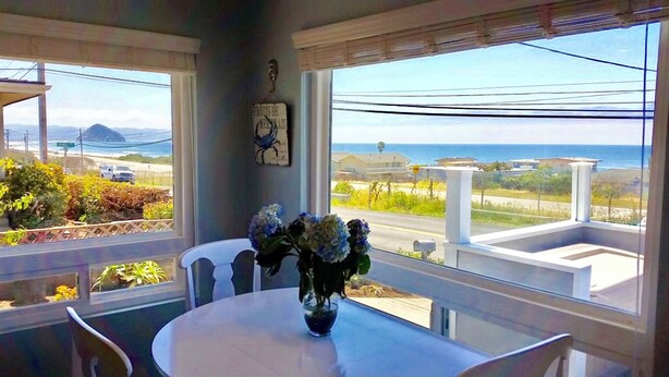 A room with a view of the ocean, a table with a vase of flowers, and a clock on the wall. - FULL OCEAN VIEW!!! 3 minute walk to beach, WiFi, Dogs welcomed upon approval (Cayucos)