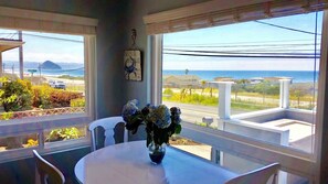 A room with a view of the ocean, a table with a vase of flowers, and a clock on the wall.