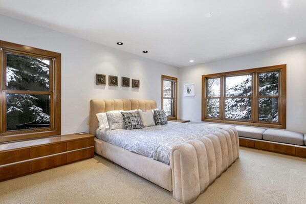 Une chambre dotée d’un grand lit, de banquettes intégrées et de grandes fenêtres offrant une vue sur un paysage enneigé.