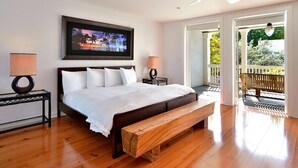 Une chambre à coucher avec un lit, un banc, un téléviseur fixé au mur et un balcon donnant sur un paysage verdoyant.