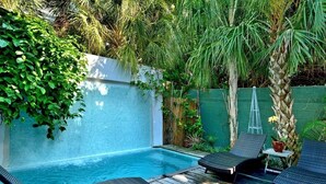Un espace piscine privé, agrémenté de chaises longues et d’une petite table, entouré d’une végétation luxuriante et d’un mur blanc.