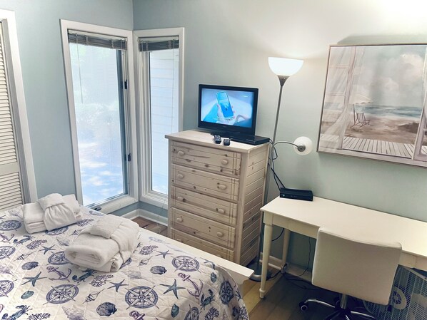 A hotel room with a bed, a desk, a TV, a lamp, and a painting of a beach scene.
