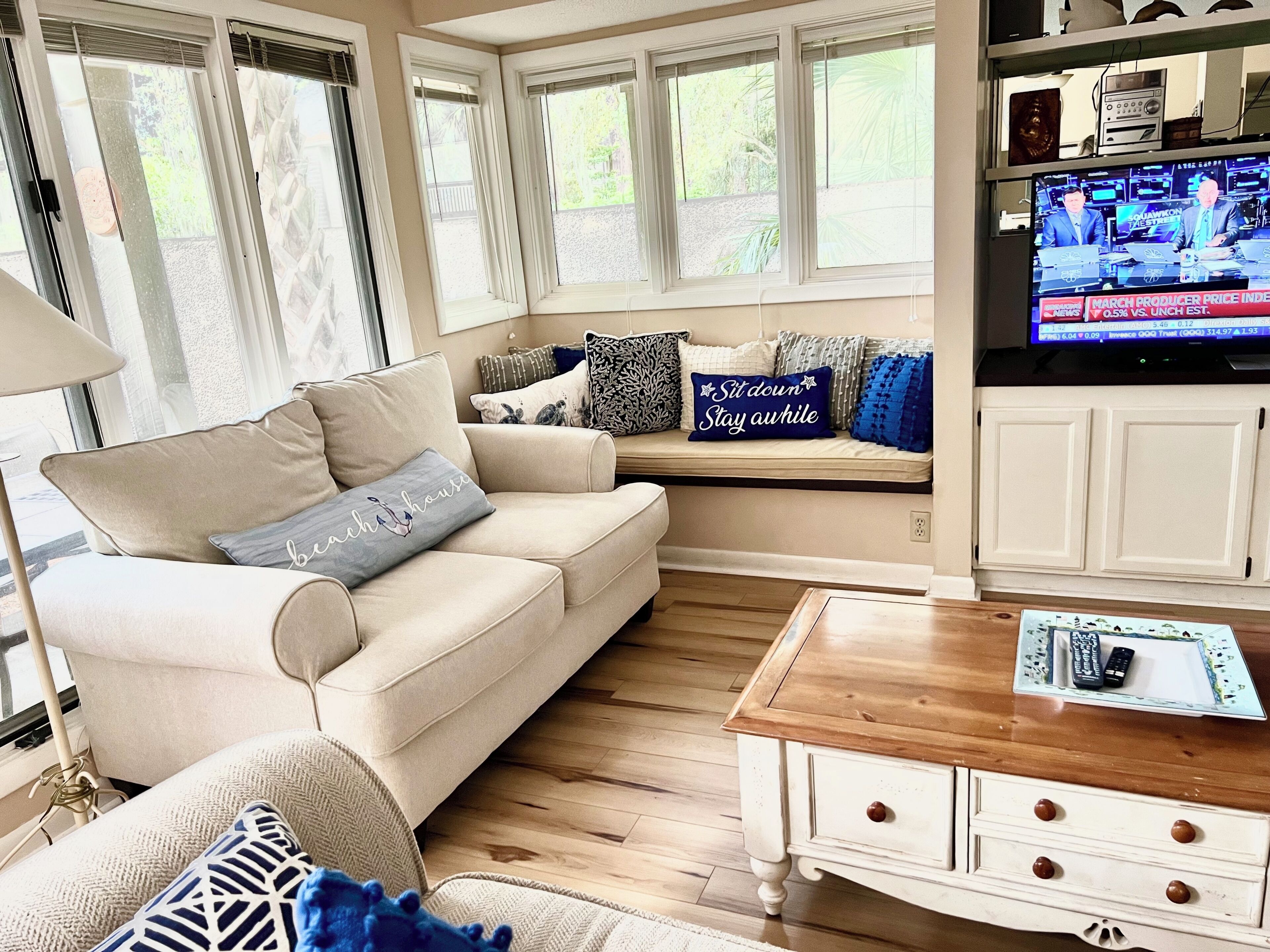 A living room with a beige sofa, a wooden coffee table, and a television displaying a news channel.