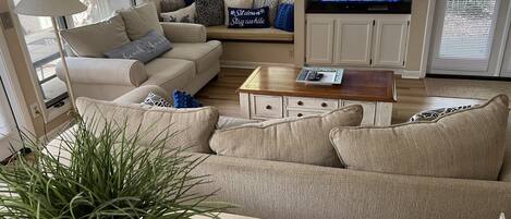 A living room with a beige sofa, a coffee table, and a television displaying a news program.