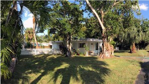 A house with a white picket fence, surrounded by lush greenery and trees. - Tropical painter and writer retreat (Jensen Beach)