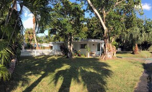 A house with a white picket fence, surrounded by lush greenery and trees.