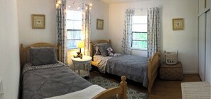 A second bedroom with two single beds, a small round table, and a window with curtains.
