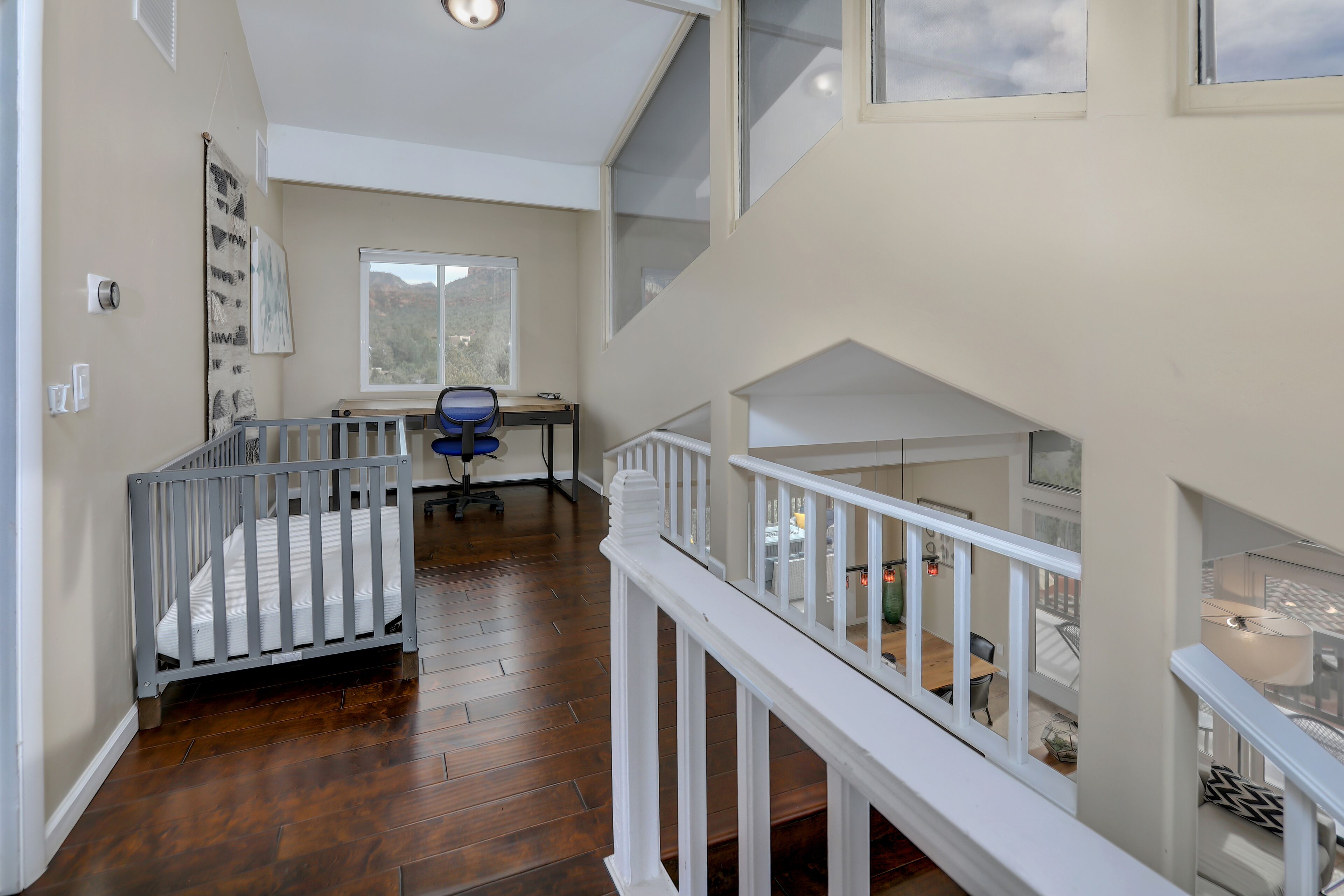 A spacious room with a wooden floor, a desk with a chair, a crib, and a staircase with a railing.