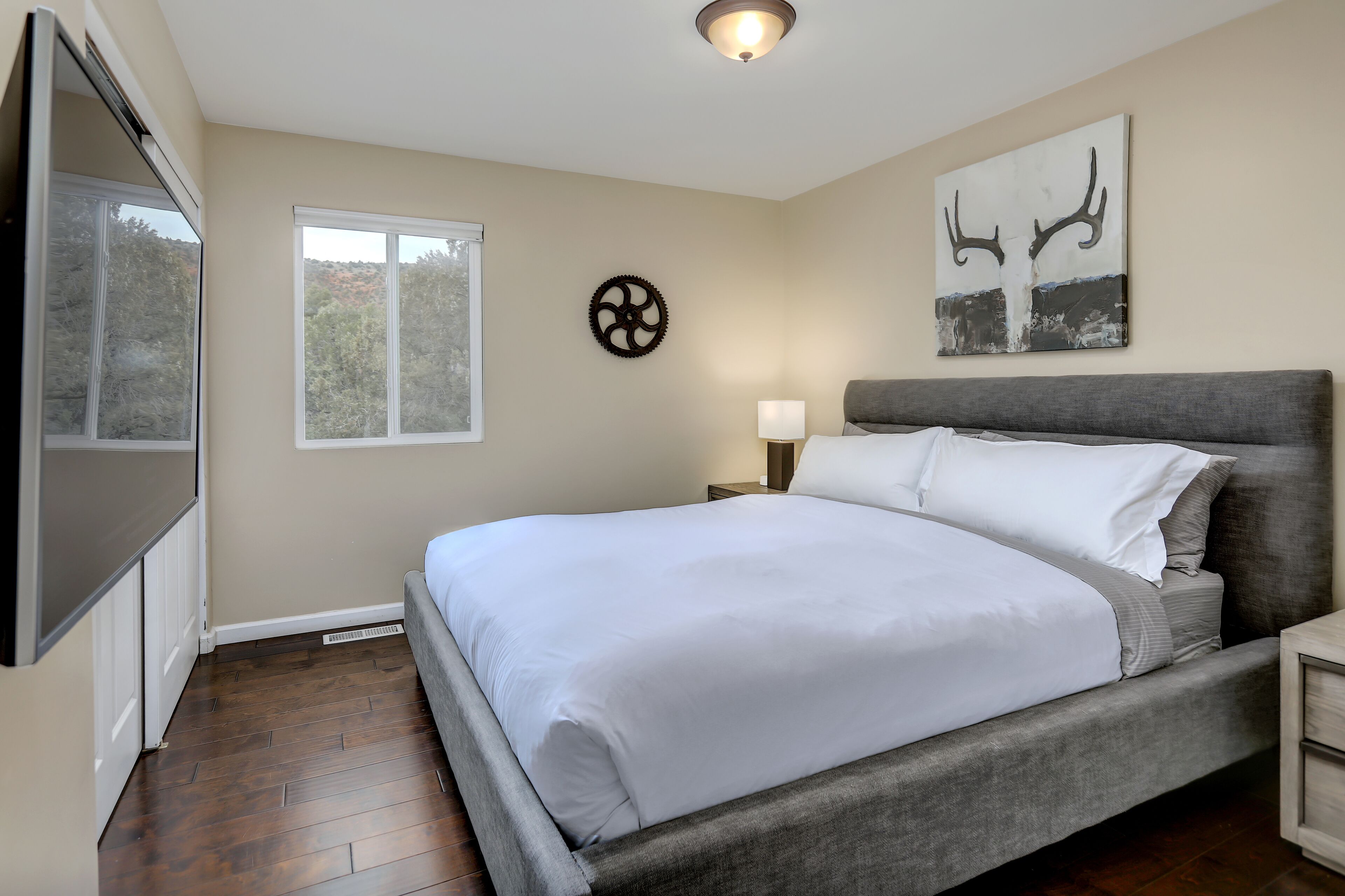 A bedroom with a large bed, a TV, a window, and artwork on the wall.