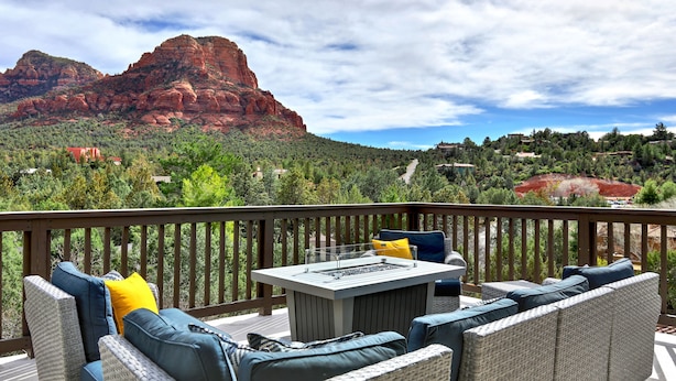 Eine Terrasse mit Korbmöbeln und einem Tisch, mit Blick auf eine gebirgige Landschaft.