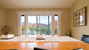 Ein Essbereich mit einem Holztisch, schwarzen Stühlen, einer weißen Tischmatte und Blick auf rote Felsformationen durch große Fenster.