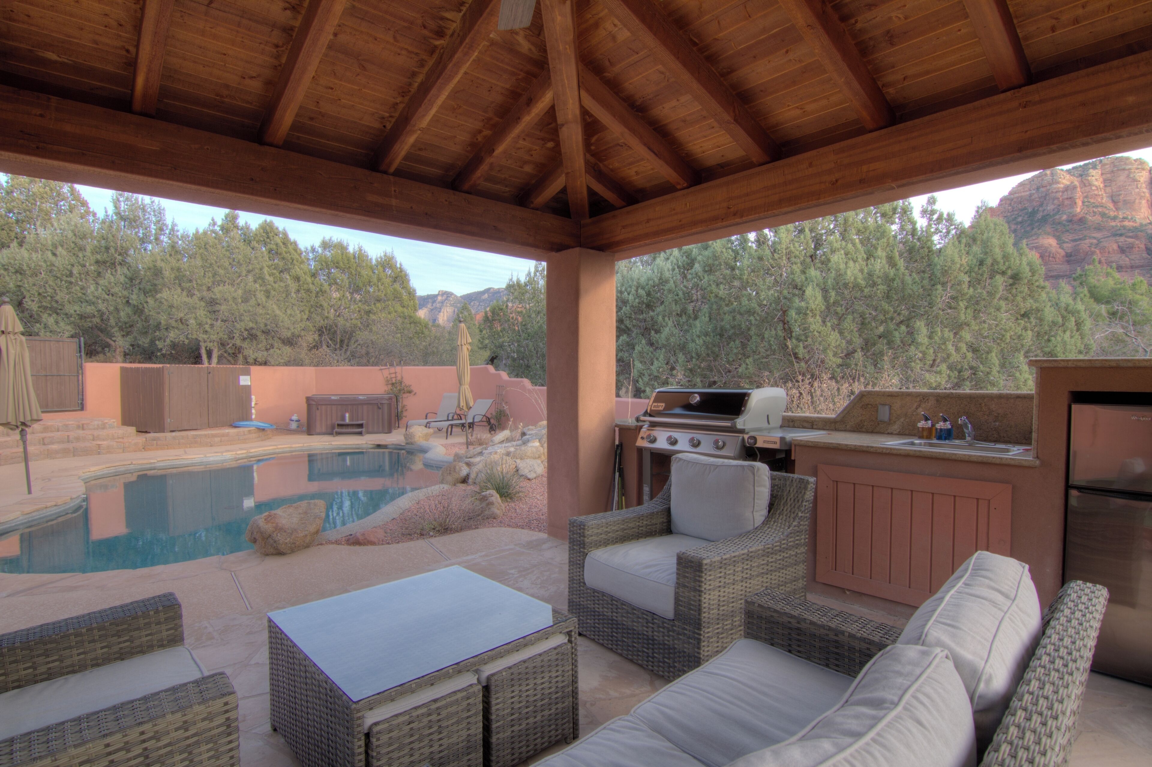 An outdoor patio with a pool, wicker furniture, a grill, and a kitchen area.