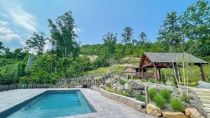 A swimming pool with a wooden deck, surrounded by a stone wall and a fence. - Mountain Sunrise- A Rustic Mountain Retreat (Gatlinburg)