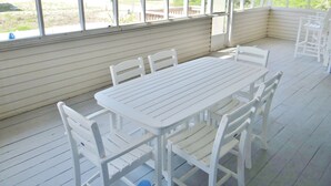 A covered patio with a white table and chairs, large windows, and a view of the outdoors. - Spacious pool home on corner lot close to beach boardwalk. Gulf view and clean! (St. George Island)