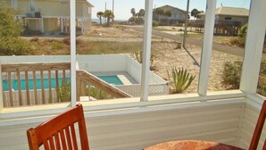 A view from a window of a room with a pool, a wooden deck, and a view of a beach and houses. - Spacious pool home on corner lot close to beach boardwalk. Gulf view and clean! (St. George Island)