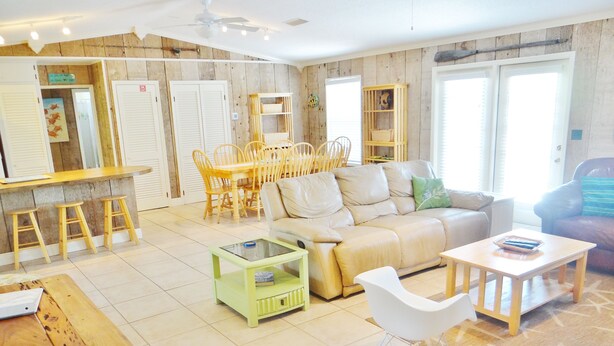 A spacious living area with a sofa, a dining table with chairs, a small coffee table, and a rocking chair. - Spacious pool home on corner lot close to beach boardwalk. Gulf view and clean! (St. George Island)