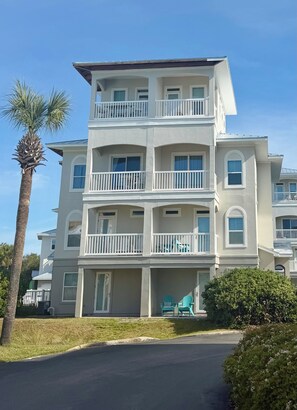A multi-story residential building with balconies, a palm tree, and a well-maintained lawn.