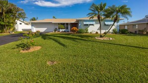 Une maison de plain-pied avec un garage, un porche à l’avant et une pelouse bien entretenue agrémentée de palmiers.