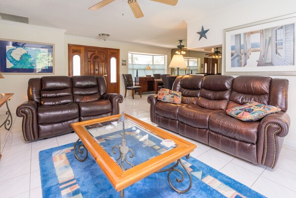 A spacious living room with two brown leather sofas, a glass coffee table, and a blue patterned rug.