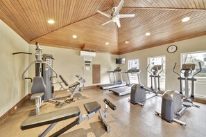 Een sportschool met diverse trainingsapparaten, een plafondventilator en een klok aan de muur.
